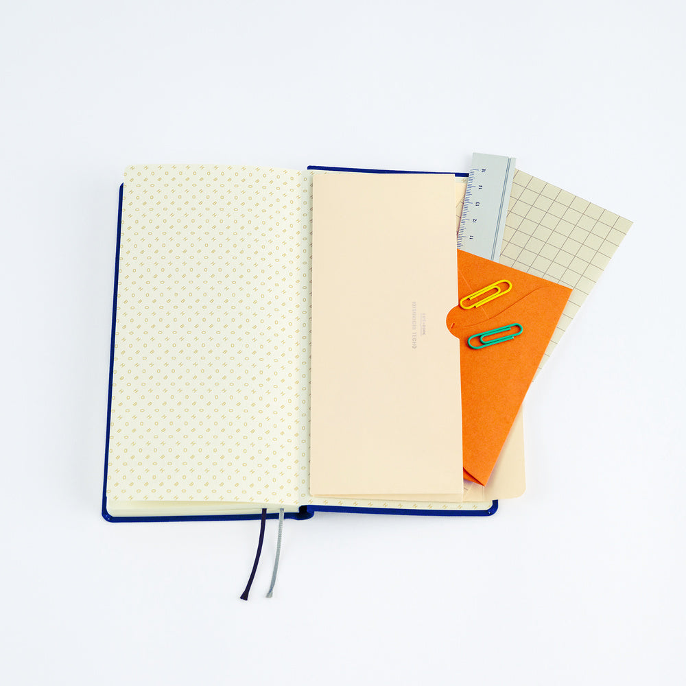 An open Hobonichi Techo Weeks planner with a cream paper pocket envelope open with stationery supplies on white background