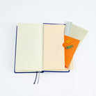 An open Hobonichi Techo Weeks planner with a cream paper pocket envelope open with stationery supplies on white background