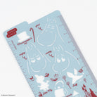 A light blue plastic craft stencil sheet featuring red and white line-art illustrations of Moomin characters and facial expressions, with measurement markings along the right edge.