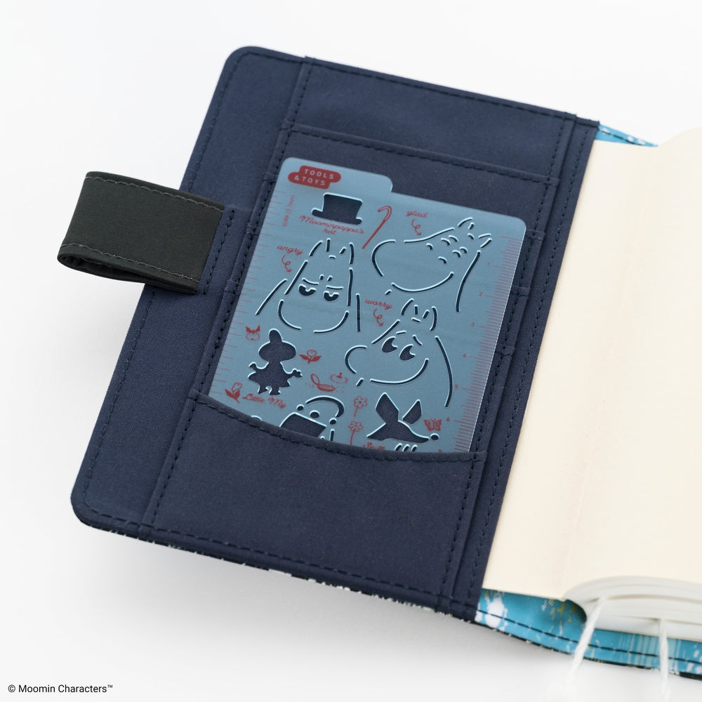 A navy blue notebook cover featuring a pocket with Moomin-themed stencil with character cutouts, shown open on a white background.