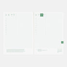An open planner or notebook showing two white grid pages with a minimalist green and gray layout, photographed on a light gray background.