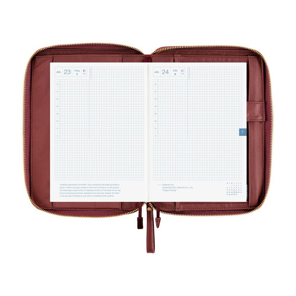 An open wine-colored A5 Hobonichi zippered cover holding a gridded planner, with interior pockets, pen holder, and gold zipper visible on a plain white background.