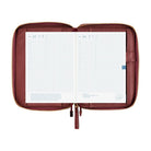 An open wine-colored A5 Hobonichi zippered cover holding a gridded planner, with interior pockets, pen holder, and gold zipper visible on a plain white background.