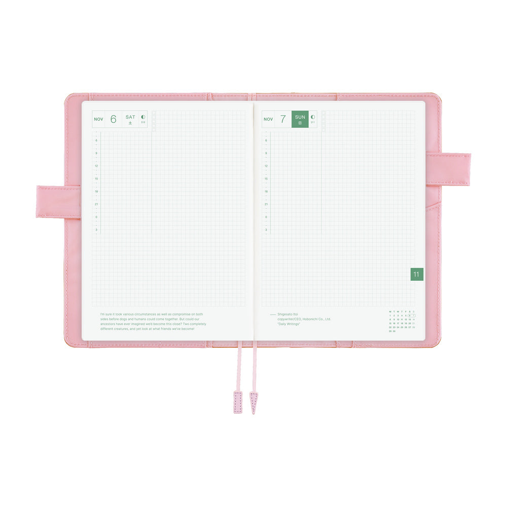 An open pink planner with white grid pages, ribbon bookmarks, and side loops, photographed on a clean white background.