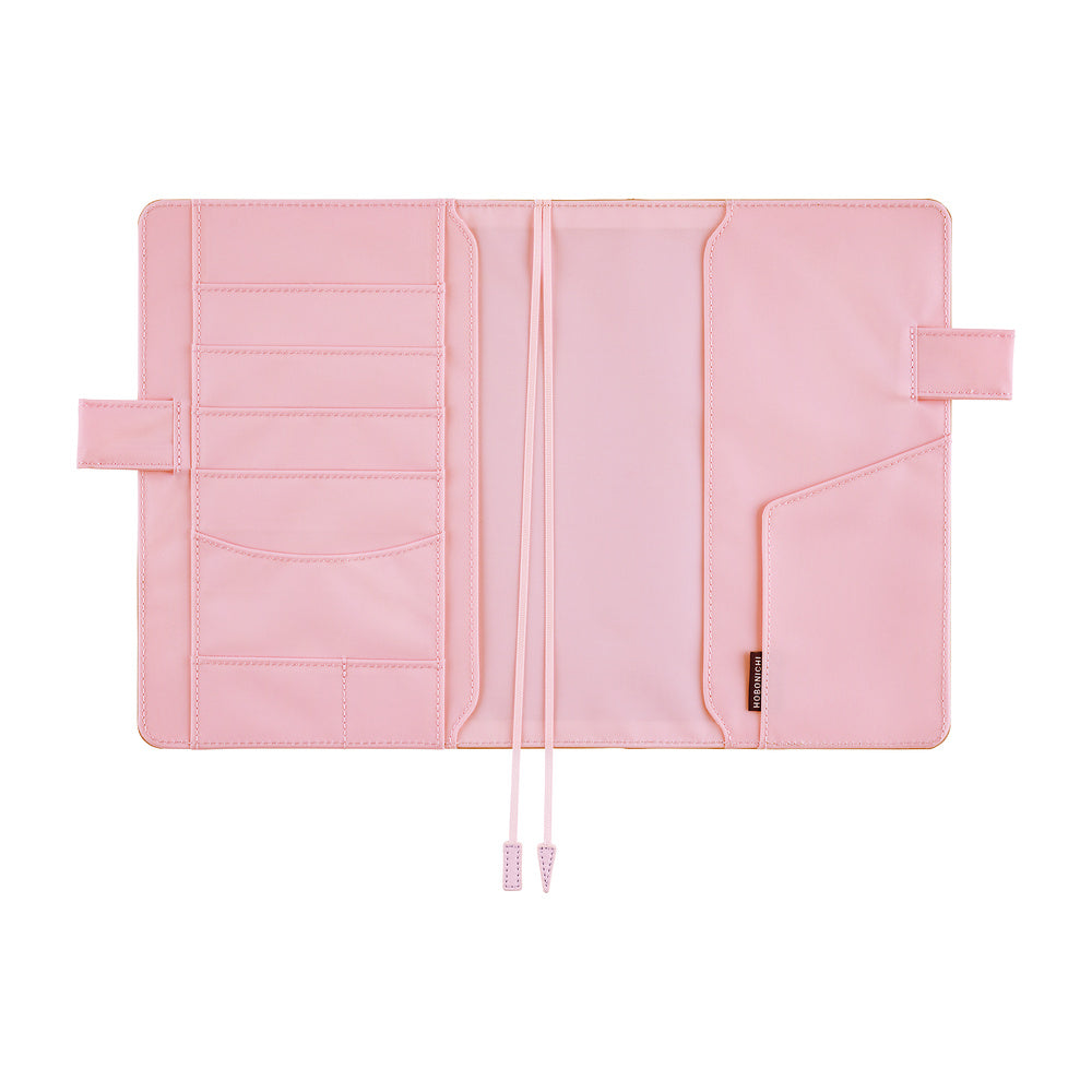 Pink interior of a Hobonichi Techo cover laid open flat on a white background, showing multiple card and storage pockets, pen loops, and two ribbon bookmarks.