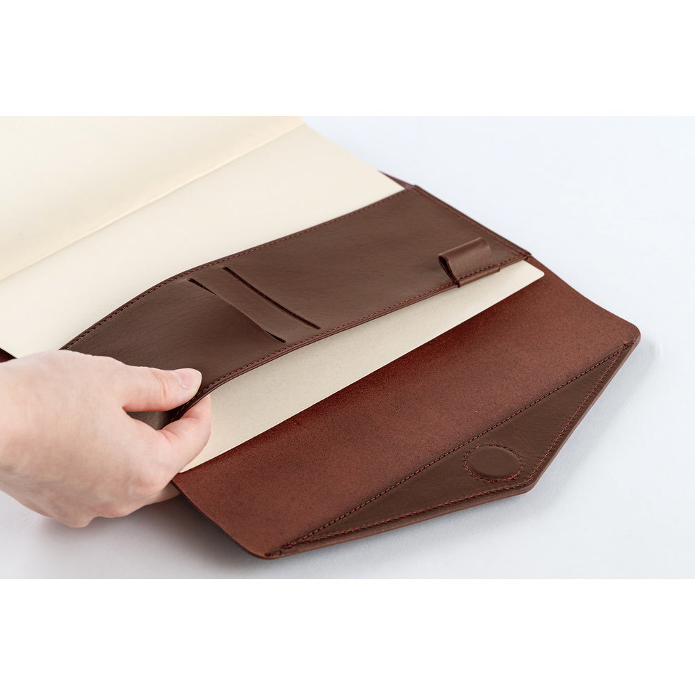 A hand inserting a Hobonichi Techo into a brown leather Hobonichi Techo cover.