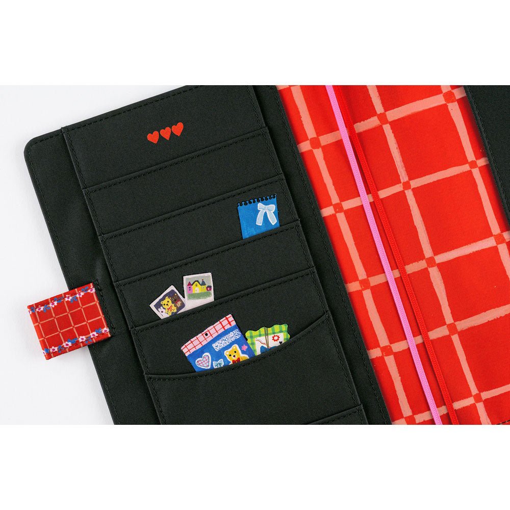 The left interior of a Hobonichi Techo cover featuring black fabric pockets decorated with whimsical illustrations and red accents.