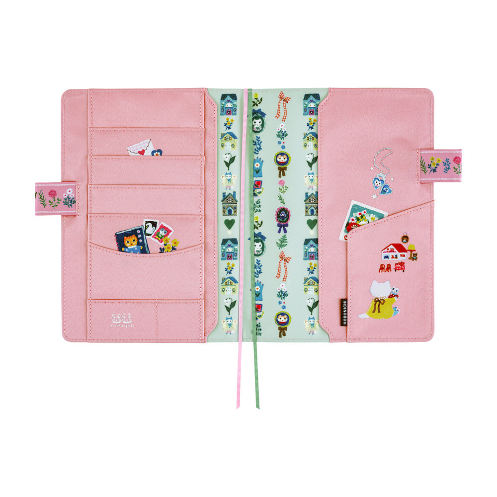 Interior of pink planner cover shown open on a white background, featuring multiple card slots, pockets, and whimsical illustrations of animal characters, houses, and flowers. 