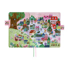 A colorful illustrated notebook or journal cover featuring a whimsical village scene with houses, trees, flowers, and small characters on a pink background, shown against a plain white backdrop.