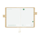 An open grid planner with white pages and an ivory interior cover, featuring  ivory pen loop closures and ribbon bookmarks, shown on a solid white background.