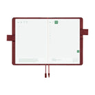 An open planner with white grid pages and a dark reddish-brown interior cover, shown on a plain white background. The cover has a pen loop on both sides and two ribbon bookmarks hanging from the bottom center.