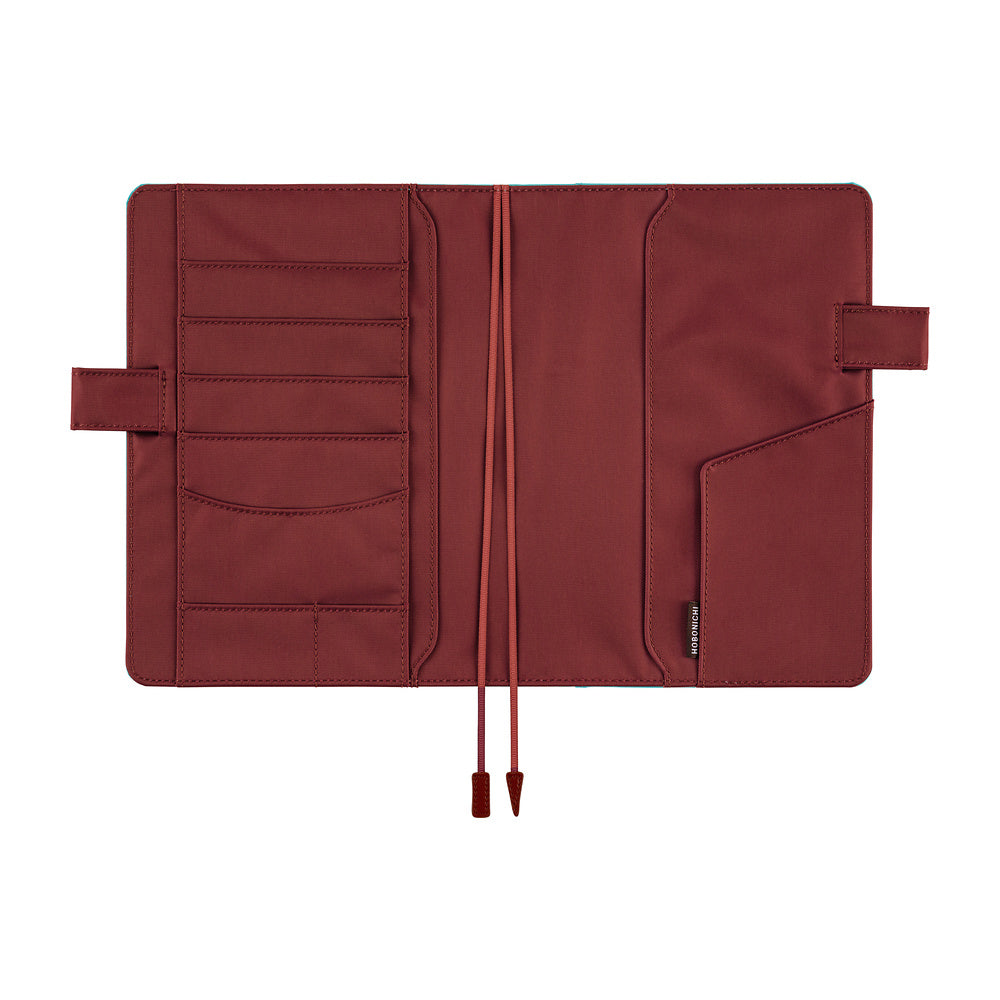 A dark red brown notebook cover shown open, featuring multiple card slots, a pocket, and ribbon bookmarks photographed against a solid white background.