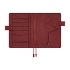A dark red brown notebook cover shown open, featuring multiple card slots, a pocket, and ribbon bookmarks photographed against a solid white background.