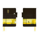 Two side by side views of yellow and black planner cover featuring a graphic of an airport with a glowing yellow window and a sign with the number 8. The notebook has two yellow ribbon bookmarks and is shown against a solid white background.