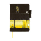 A black planner cover featuring a printed graphic of an airport with a glowing yellow window and a sign with the number 8. The notebook has two yellow ribbon bookmarks and is shown against a solid white background.