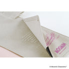Close-up interior image of a beige cover with a folded corner revealing printed text and a pink line-art illustration. The word 'MOOMIN' is printed in pink on the inside.