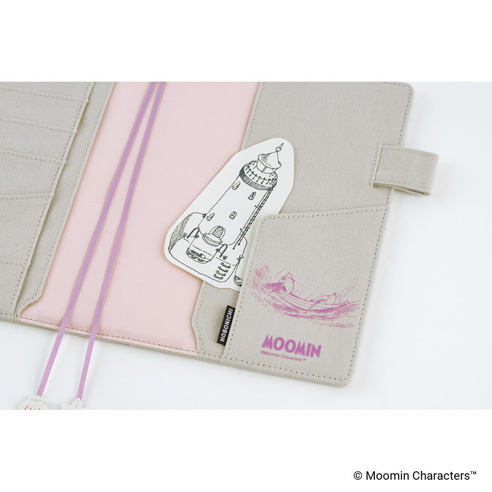 A close-up of the planner cover with a pink interior lining, a lighthouse illustration sticker, and a pink Moomin logo on the pocket.