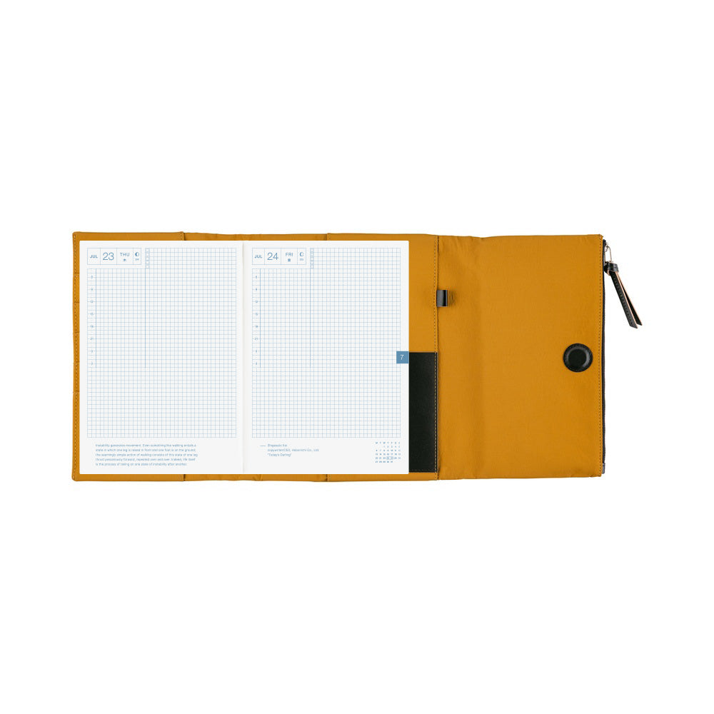 An open mustard yellow Hobonichi Tragen tri-fold cover holding a gridded planner, with interior pockets, pen holder, magnetic closure, and zippered pouch visible on a plain white background.