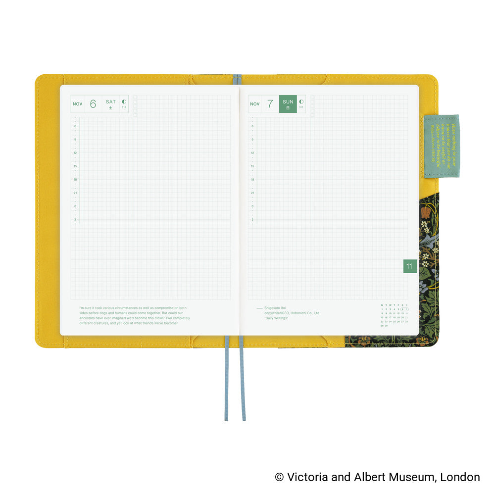 An open planner with a bright yellow interior cover, white grid pages, blue ribbon bookmarks, and a decorative patterned page edge, shown on a white background.