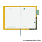 An open planner with a bright yellow interior cover, white grid pages, blue ribbon bookmarks, and a decorative patterned page edge, shown on a white background.