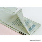 A close-up of a pale sage green fabric accessory, likely a pouch or strap, with stitched edges, printed blue text and illustration, and a small black brand tab reading Moomin. The fabric is photographed on a clean white background with a soft pink area visible underneath.