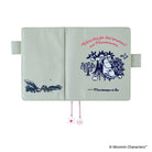 A Moombaapapa & Sea character-themed notebook or planner cover shown open against a white background. The cover is a pale sage green with navy blue illustrations of a forest scene on the left page and a character illustration with pink text on the right page.