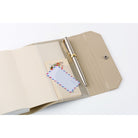 A beige notebook holder shown open on a white background, containing a clear plastic pocket with a silver pen and a postcard.