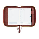 An open brown leather planner or organizer pouch with gold-tone zippers, displaying two white grid calendar inserts on a plain white background.