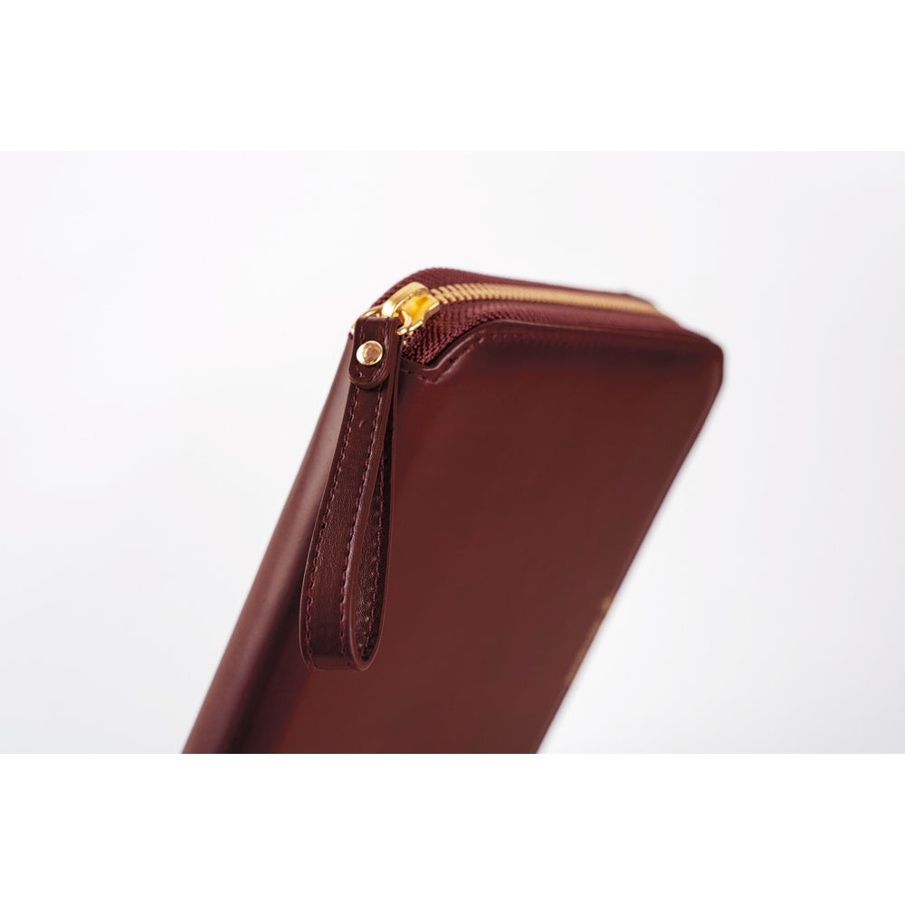 A close-up of a dark reddish-brown leather zip-around notebook with a gold-tone zipper and a small leather pull tab, shown against a plain white background.