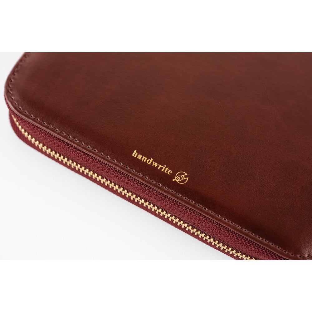 A close-up of a burgundy leather journal. There is a close up of the word "handwrite" in gold writing