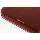 A close-up of a burgundy leather journal. There is a close up of the word "handwrite" in gold writing