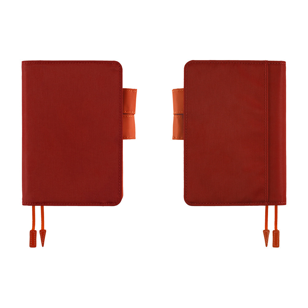 Two red leather planner covers shown side by side on a plain white background, each with a small orange-brown tab and matching red ribbon bookmarks.