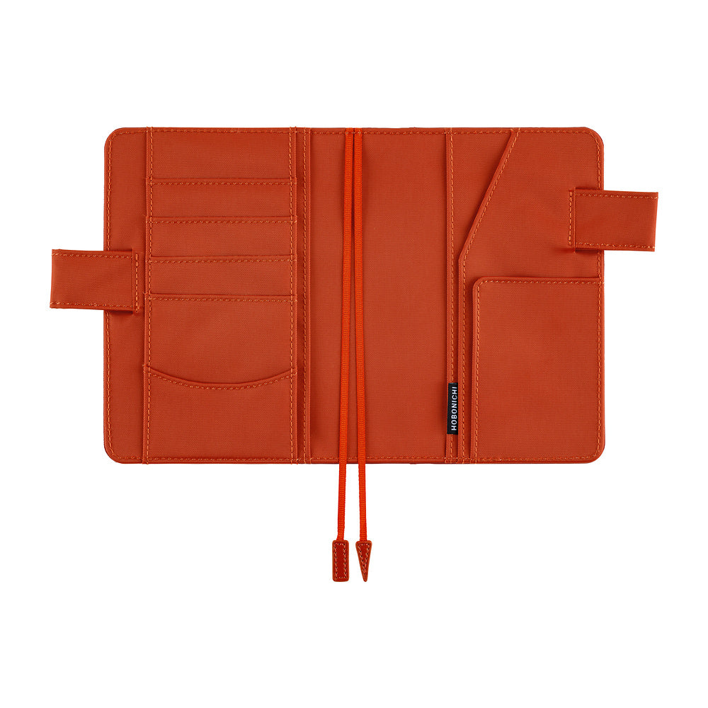 An orange-brown leather notebook cover shown open, featuring multiple card slots, a pocket, a strap closure, and a drawstring detail, photographed on a solid white background.