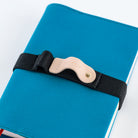 A close-up of a blue notebook or journal secured with a black elastic strap and a beige leather buckle. The buckle has the brand name 'Handwrite' embossed on it.