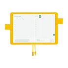 A yellow grid planner insert or pocket organizer shown open on a white background, with two yellow tabs extending from the sides and two hanging yellow cords at the bottom. The insert features light gray grid lines and small green date blocks.