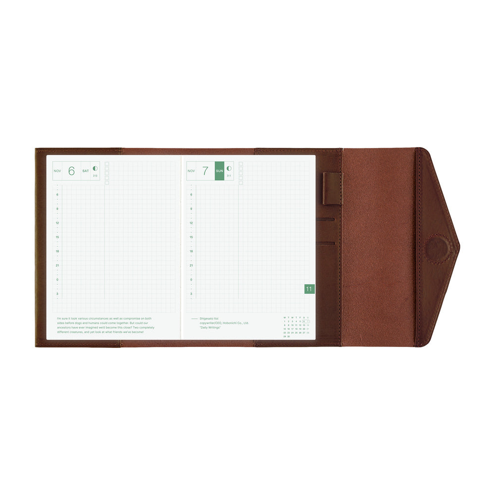 A brown leather planner cover shown open, displaying two white grid planner inserts with green accents on a plain white background.
