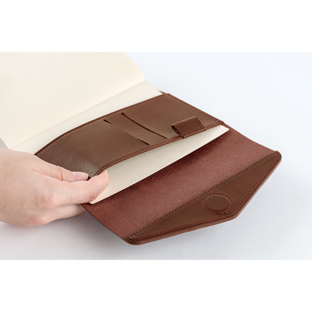 A hand holding open a brown leather notebook cover or document holder, showing cream-colored interior pages and card slots, on a clean white background.