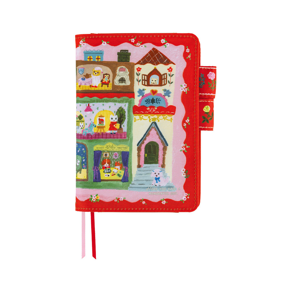 A red hardcover notebook or journal featuring a colorful cartoon village illustration on the cover, with ribbon bookmarks in pink and red, shown on a plain white background.