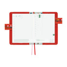 An open red leather planner with grid pages, floral strap details, and two ribbon bookmarks, photographed on a clean white background.