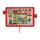 A children's fabric book or activity book featuring a colorful embroidered village scene on the cover, with a red border and ribbon tabs hanging from the bottom center, shown on a plain white background.