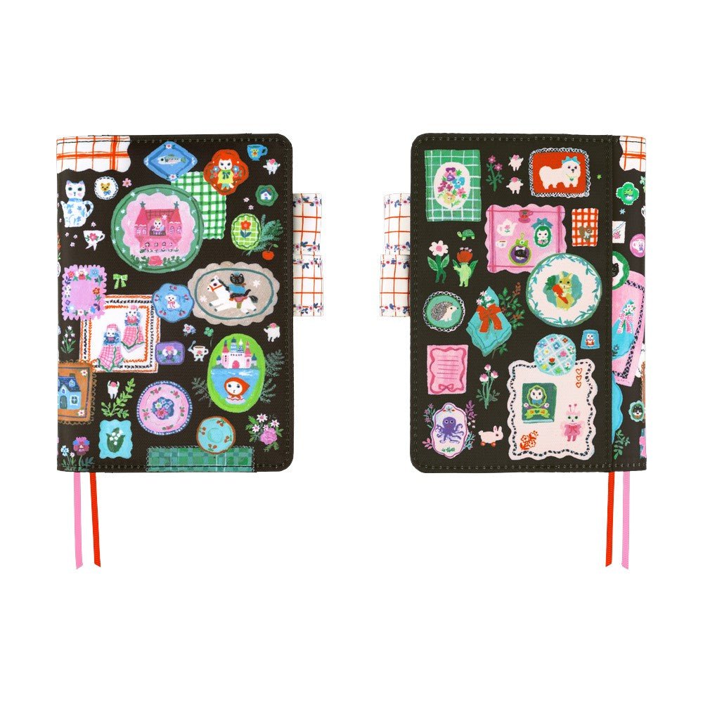 Hobonichi A6 planner cover featuring Yumi Kitagishi’s whimsical “White Cat’s Table Decorations” artwork, with a white cat-shaped teapot, teacup, colorful flowers, ribbon-tied napkin, and other cheerful tableware illustrations.
