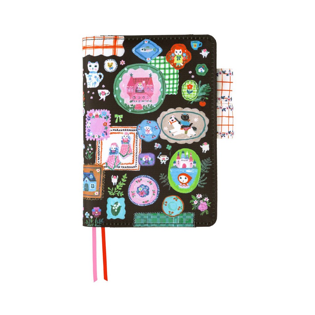 A black A6 Hobonichi notebook cover decorated with a whimsical patchwork of colorful illustrations, including houses, animals, flowers, and geometric patterns. It features a pink and red striped ribbon bookmark hanging from the bottom.