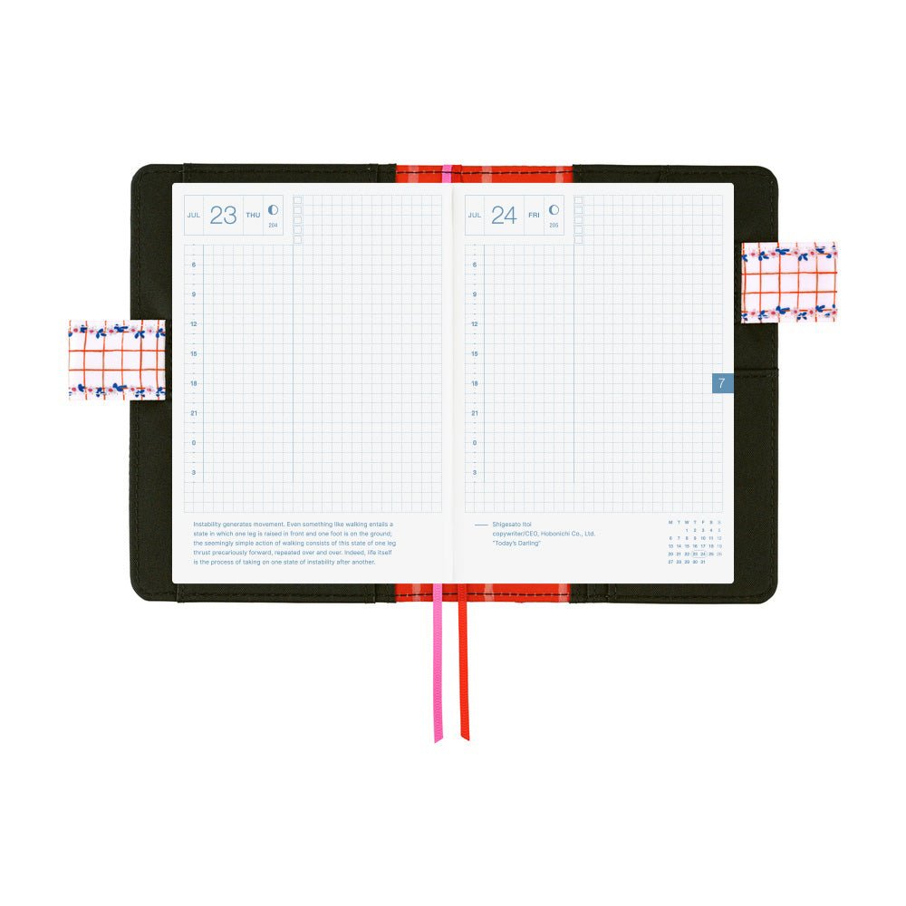 An open weekly planner with two grid pages showing days 23 and 24, a black cover, and ribbon bookmarks in red and pink, photographed on a white background.