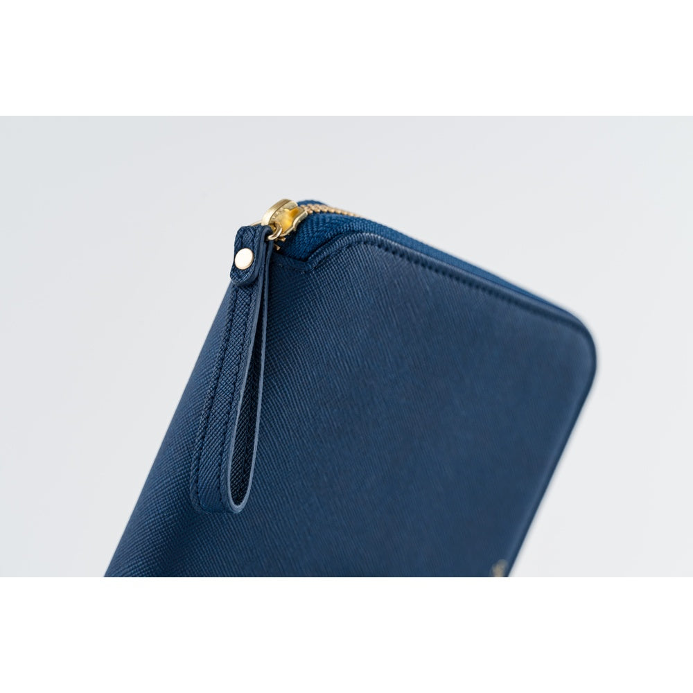 A close-up of a navy blue textured zip-around notebook case with a gold-tone zipper pull and a matching wrist loop, set against a light gray background.