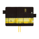 A black notebook with a printed illustration of a yellow-lit building exterior and interior, shown open against a white background. Two yellow ribbon bookmarks extend from the bottom.