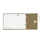 An open weekly planner with white grid pages on the left and a closed olive green cover on the right, featuring a circular snap button and a small pink pull tab with a gold zipper pull, shown on a white background.