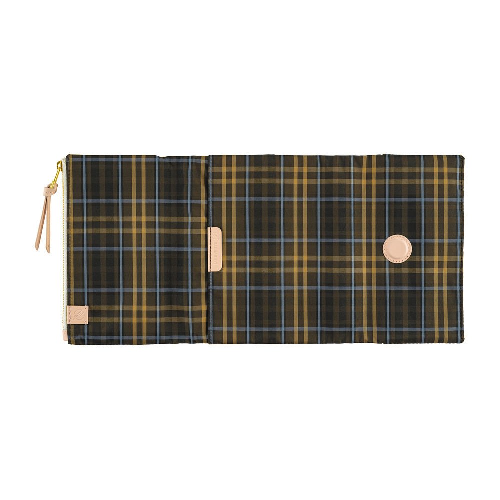 A plaid canvas pouch with a dark green, brown, and gold pattern, featuring a tan zipper pull and a circular tan snap button, shown against a plain white background.