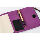 A purple notebook cover shown open on a white background, containing a black card holder, a gold and black pen, and a black circular snap button.
