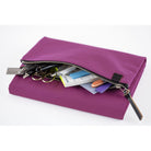 An open zippered pouch on a purple Hobonichi Tragen cover filled with pens, scissors, tape, and other stationery accessories on a white background.