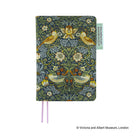 A hardcover journal featuring a detailed William Morris-style floral and bird pattern in muted green, blue-gray, and ochre tones, with two pink ribbon bookmarks and a small light green paper tag on the right side.